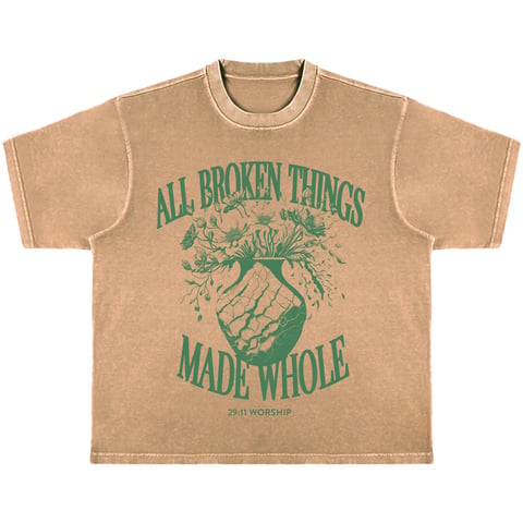 Tan vintage-style t-shirt with green graphic design reading All Broken Things Made Whole featuring an artistic plant design